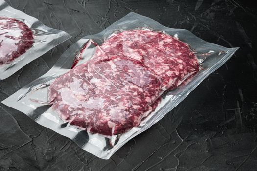 Raw fresh beef burgers minced meat in plastic tray set, on black stone background, with copy space for text