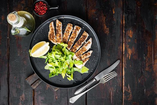 Crumbed, chicken breast fillet grilled, on wooden table, flat lay with space for text