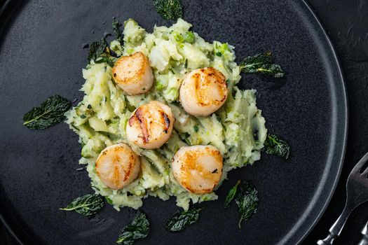 Cooked scallops with mushed minty potatoes and green pea, top view, on black textured background