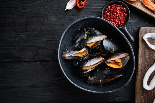 Steamed mussels over black wood table, flat lay with copy space, food photo.