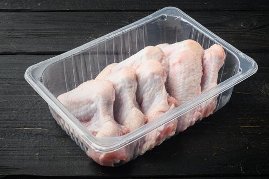 Fresh chicken wings spit in plastic vacuum pack set, on black wooden table background