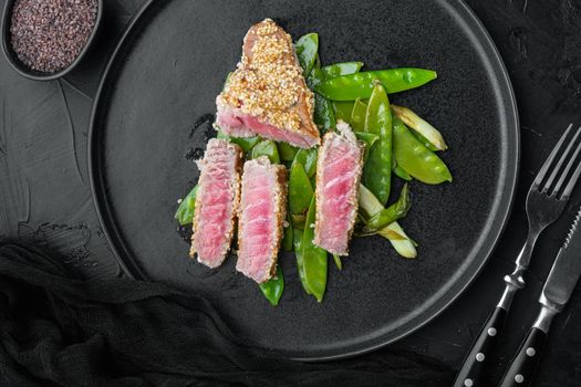 Grilled red rare tuna steak with spring onions and sugar snap peas set, on plate, on black stone background, top view flat lay