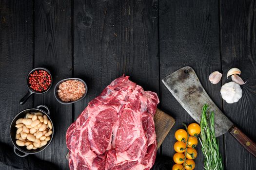 Raw rib eye beef marbled meat steak with pepper and herbs set, and old butcher cleaver knife, on black wooden table background, top view flat lay, with copy space for text