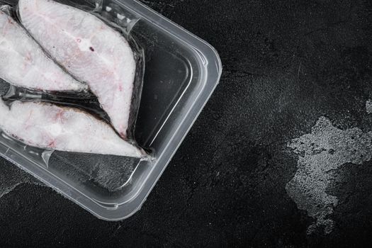 Halibut fish frozen steak pack set, on black dark stone table background, top view flat lay, with copy space for text