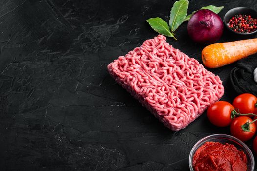 Preparing Bolognese sauce ingredients, minced meat, tomatoe, herbs set, on black stone background, with copy space for text