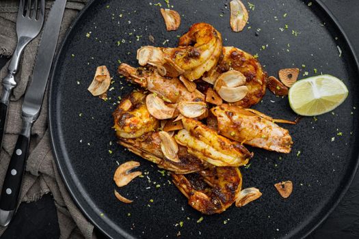 Delicious roasted shrimps with garlic, curry and mango sauce set, on plate, on black background, top view flat lay