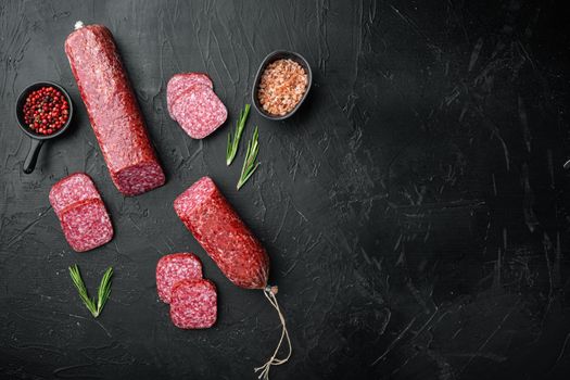 Slices of salami with vegetables set, on black dark stone table background, top view flat lay, with copy space for text