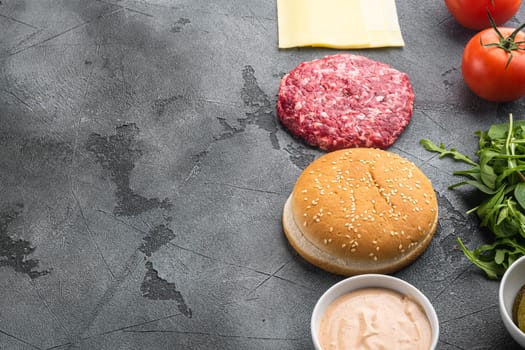 Ingredients for cooking burgers. Minced beef patties, buns, tomatoes, herbs and spices set, on gray stone background, with copy space for text