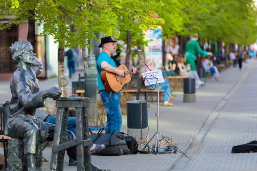 An adult gray-haired man plays guitar and sings on a city street. Street musician. Chelyabinsk, Russia, May 17, 2021