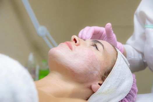 A young woman is wiped off traces of blood from a plasma injection on her face. Plasmolifting. Apply cream.