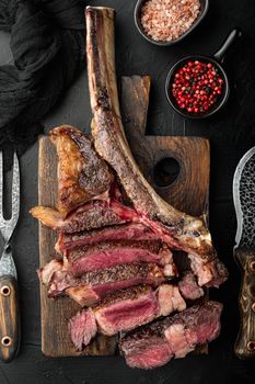 Fresh grilled meat. Grilled beef steak medium rare set, tomahawk cut, on wooden serving board, on black stone background, top view flat lay