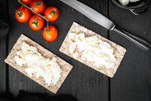Wholegrain Rye Crispbread with cream cheese set, on black wooden table background, top view flat lay