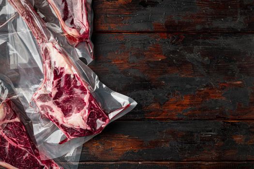 Dry aged steak in a vacuum. Meat products in plastic pack set, tomahawk, t bone and club steak cuts, on old dark wooden table background, top view flat lay, with copy space for text