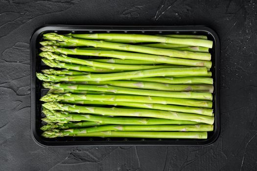 Bunches of fresh green asparagus set, in plastic market container, on black stone background, top view flat lay