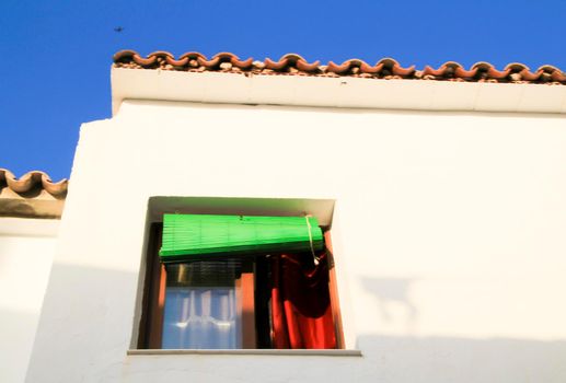 Whitewashed facade with window with green wooden blind in Altea village, Alicante, Spain