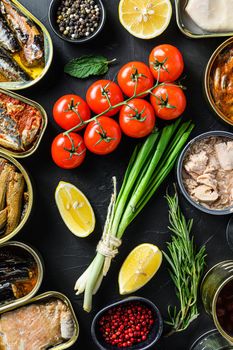 Mix of canned preserves food in cans with fresh organic bio ingredients tomatoe herbs lemon On the black chalkboard. Top view concept.