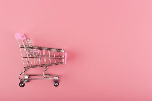 Creative flat lay with top view of toy shopping cart on pink background with copy space. Concept of online retail, sales and shopping. Template for commercial or advertisement