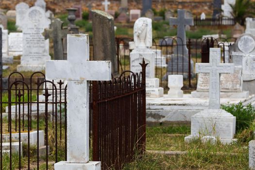 White marble stone cross headstone with various graves in an old colonial cemetery, South Africa