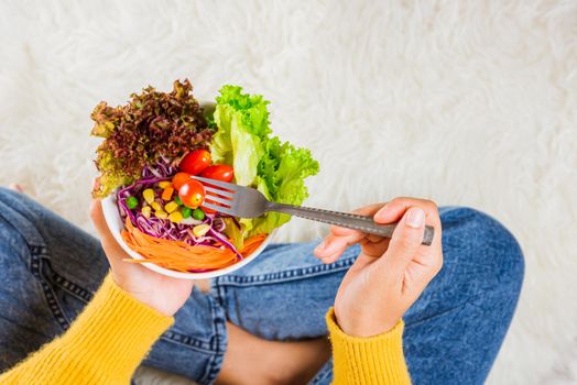 Young woman eating fresh salad meal vegetarian spinach in a bowl, top view of female hands holding bowl with green lettuce salad on legs, Clean detox healthy food concept