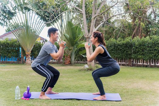 Asian young mother, father and child daughter doing exercising together with dumbbells is fun outdoors in nature a field garden park. Happy family kid sport and exercises for healthy lifestyle