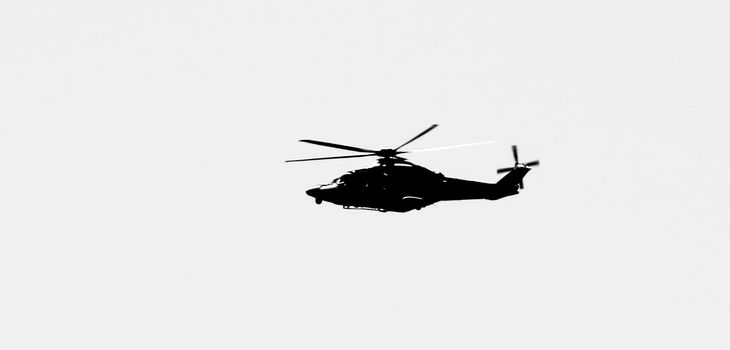 Military helicopter flying over the sky of the Spanish coast. Monochrome picture.