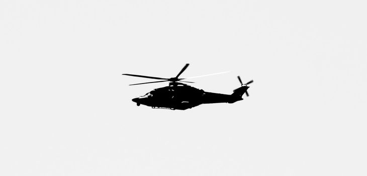 Military helicopter flying over the sky of the Spanish coast. Monochrome picture.