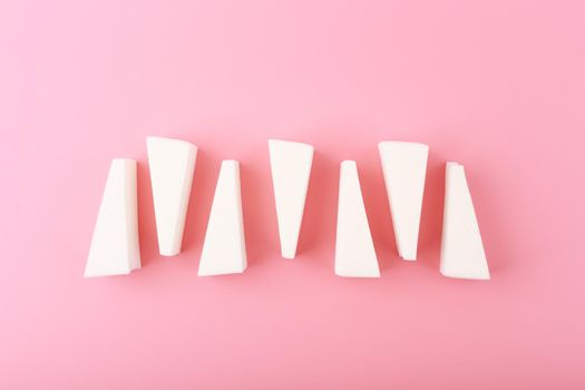 Top view of triangle shapes make up sponges in a row on bright pink background. Creative flat lay with make up sponges. Concept of beauty, make up and visage