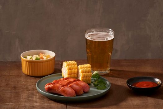 Home grilled sausages on a dark plate, a meat dish on a dark wooden background, hot sausages with spices and salt in a home kitchen, copy space, rustic style, art