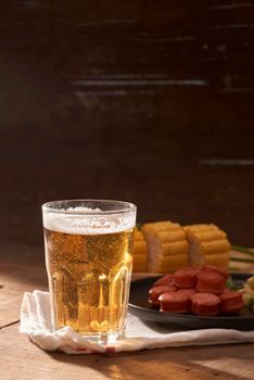 Grilled sausages with glass of beer on wooden table with copy space.