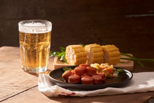 Grilled sausages with glass of beer on wooden table with copy space.