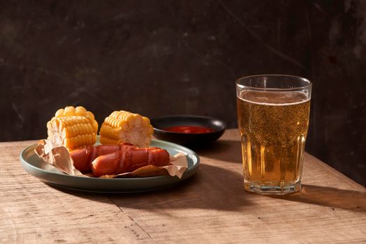 Glass of delicious beer with grilled sausages on wooden table