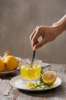 Ginger tea with lemon, ginger root and rosemarry on wooden background. Small glass transparent pitcher with hot drink. Seasonal beverages. Shallow DOF, selective focus, focus on top of pitcher.