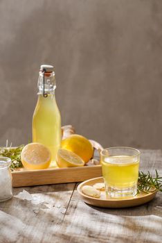 Refreshing summer drink with lemon, ginger, rosemary and ice on rustic wooden table, copy space