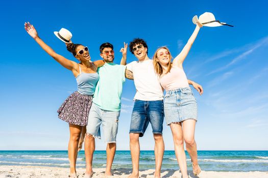 Group of multiracial young tourists posing for portrait photography in summer at tropical sea ocean resort with blue sky and crystal clear water. Happy millennial people on summer beach vacation