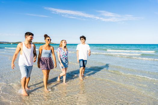 Multicultural friends walking in summer beach vacation in crystal clear water of tropical ocean sea resort smiling wearing casual clothes. Multiracial millennial happy people enjoying life in nature