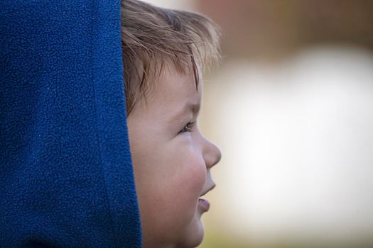 Child looking to one side and being  happy. Wearing blue hood.