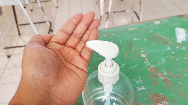 A man's hand has alcohol gel in his hand, a bottle of alcohol gel is placed next to it. Teachers wash their hands with alcohol gel before entering the classroom.