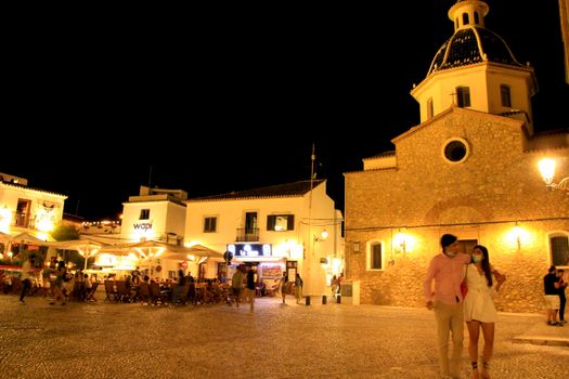 Altea, Alicante, Spain- June 12, 2021: People having drinks and enjoying nice weather in terraces in the main square of Altea village in Spain. The Virgin of the Consol church at night.