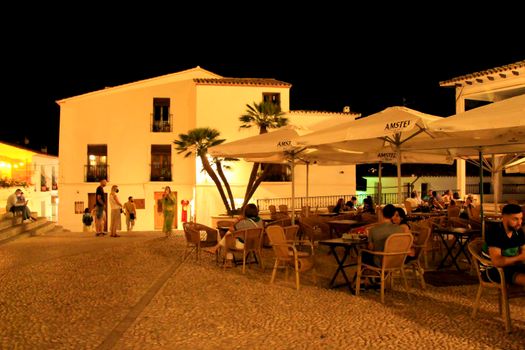 Altea, Alicante, Spain- June 12, 2021: People having drinks and enjoying nice weather in terraces in the main square of Altea village in Spain. The Virgin of the Consol church at night.