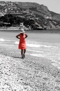 Altea, Alicante, Spain- June 12, 2021: Woman in red dress and hat on Cap Negret beach on a sunny day of Spring in Altea, Alicante, Spain
