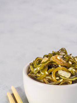 Close up view of kelp seaweed salad with sesame seeds on gray concrete background. Copy space. Vertical.