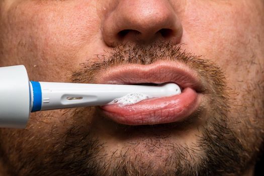 Close up of man brushing his teeth with electric toothbrush