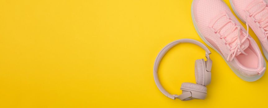 pair of pink sneakers, wireless headphones on a yellow background. Top view, copy space