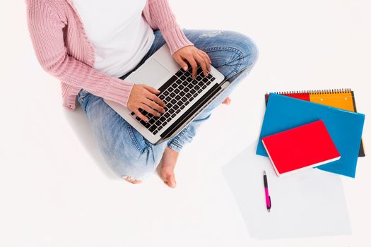 Young female student sitting with crossed legs working with a laptop, isolated over white background