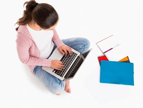 Young female student sitting with crossed legs working with a laptop, isolated over white background