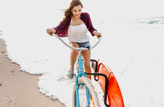 Surfer young woman riding her bicycle on the beach