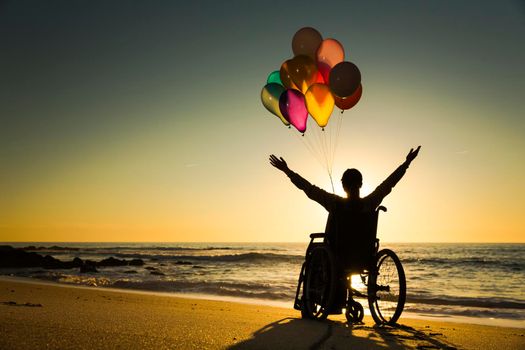 Handicapped man on a wheelchair with colored balloons at the beach