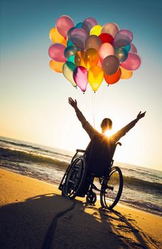 Handicapped woman on a wheelchair with colored balloons at the beach