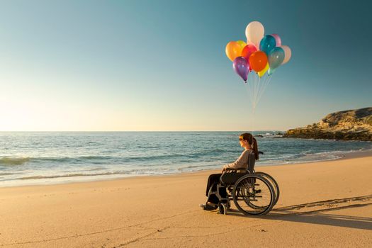 Handicapped woman on a wheelchair with colored balloons at the beach