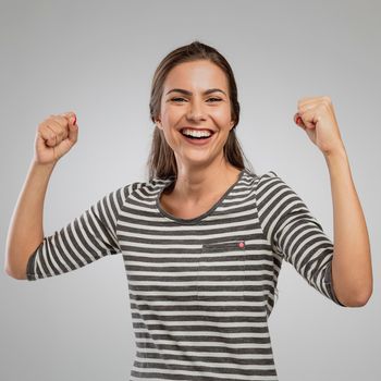 Beautiful happy woman with arms up over a gray background